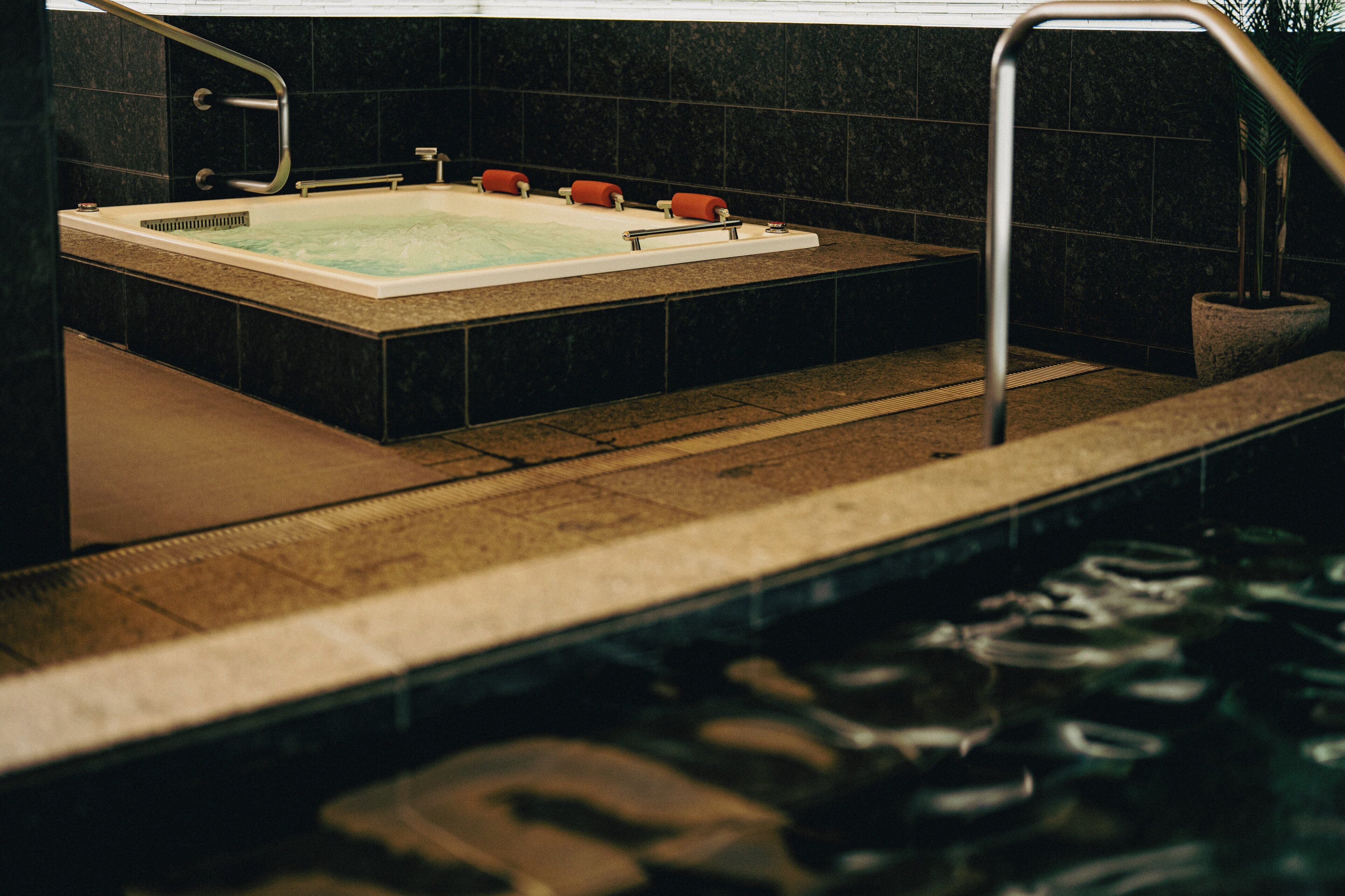 Een wellnessruimte met een jacuzzi, een douche en een betegelde vloer.