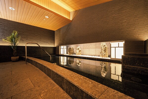 A modern indoor pool area with a wooden ceiling, stone walls, and a marble floor.