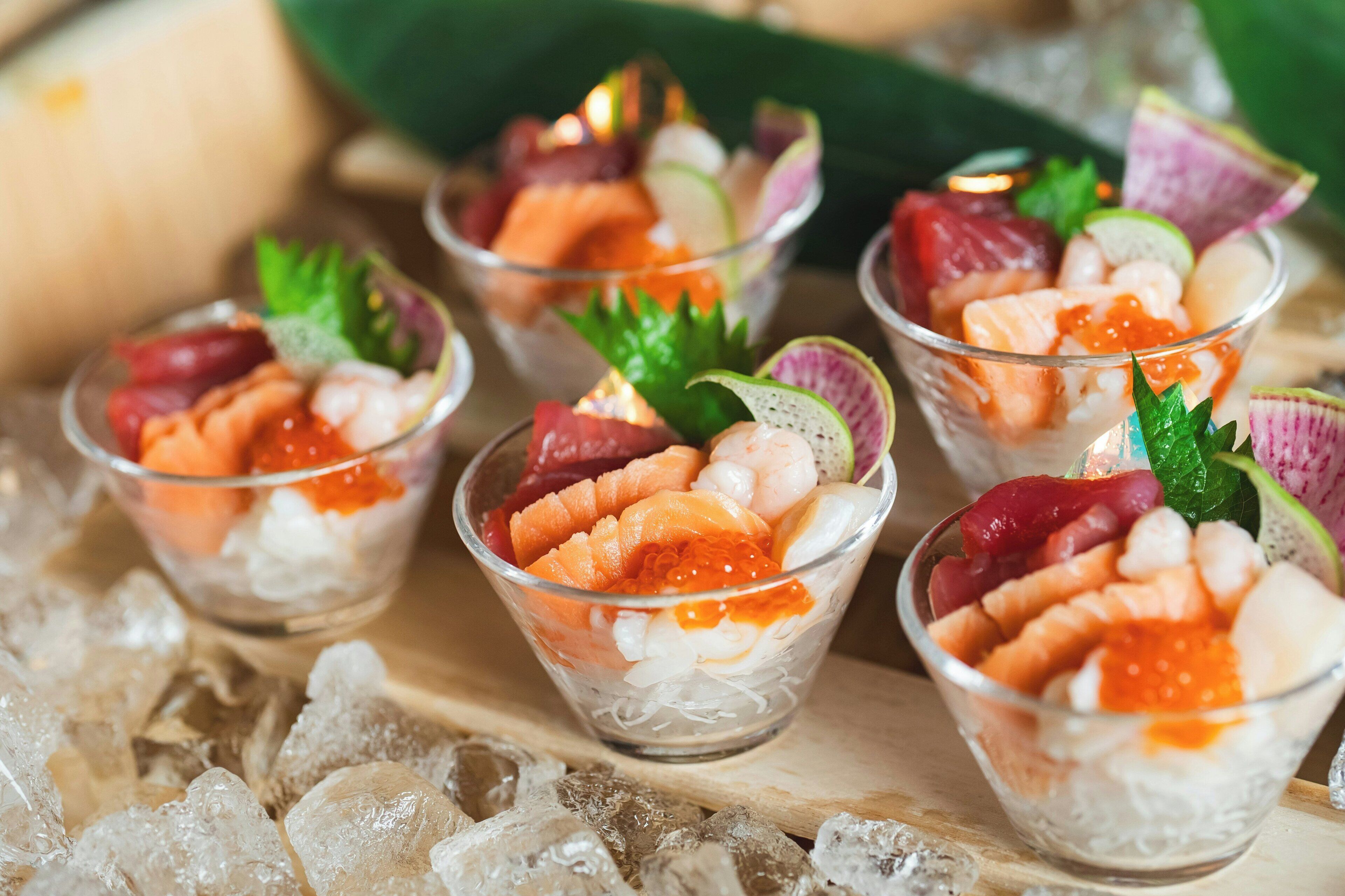 A series of clear glass cups containing a seafood dish with ice, garnished with green leaves.