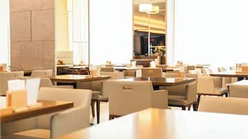 Un restaurante moderno con varias mesas y sillas, amplias ventanas y un pilar de piedra.