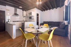Una cocina funcional con electrodomésticos modernos, un comedor con mesa de vidrio y sillas amarillas, y un sofá de color oscuro en la sala.