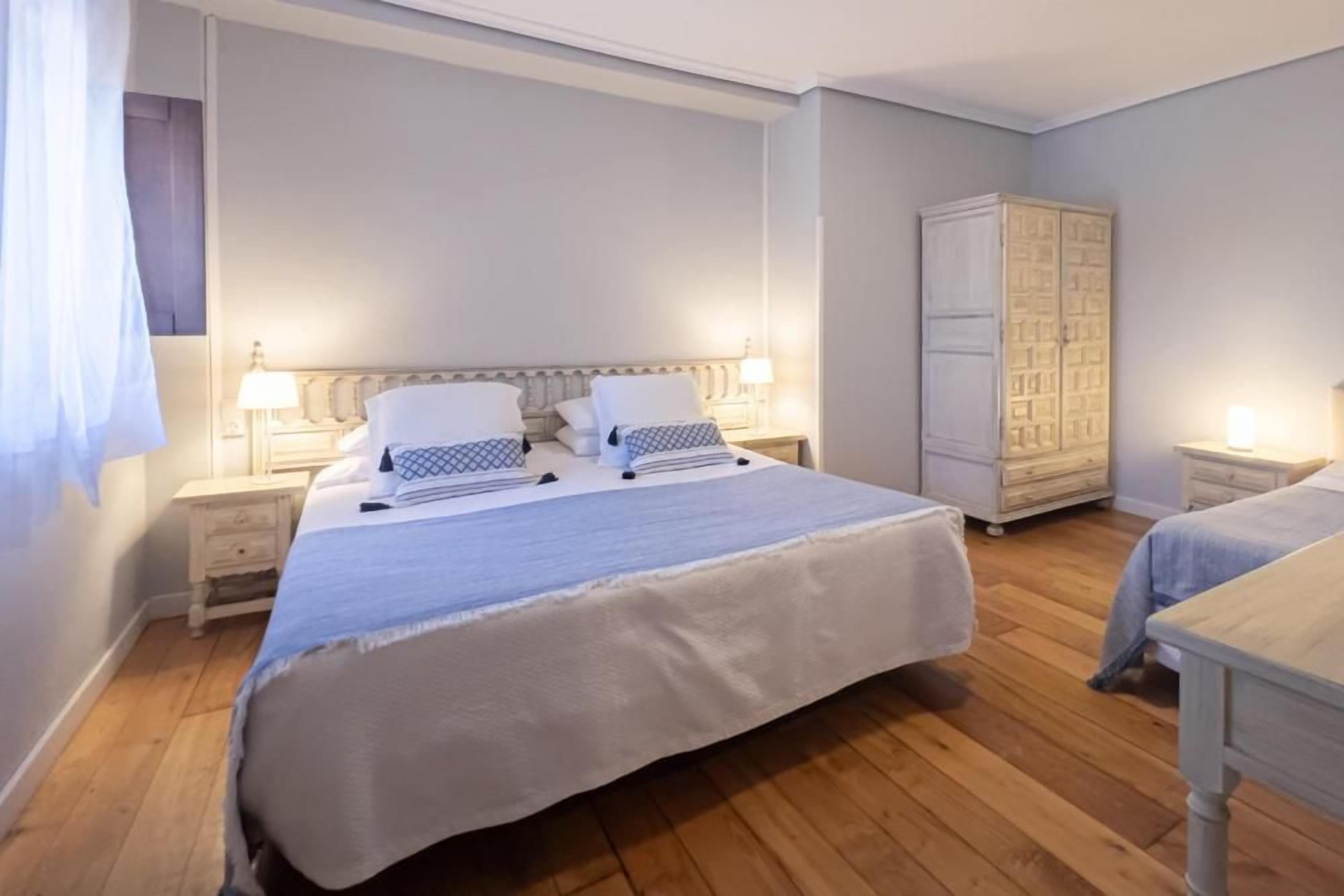 Un dormitorio con una cama grande, dos mesitas de noche, un armario y una ventana con cortinas.