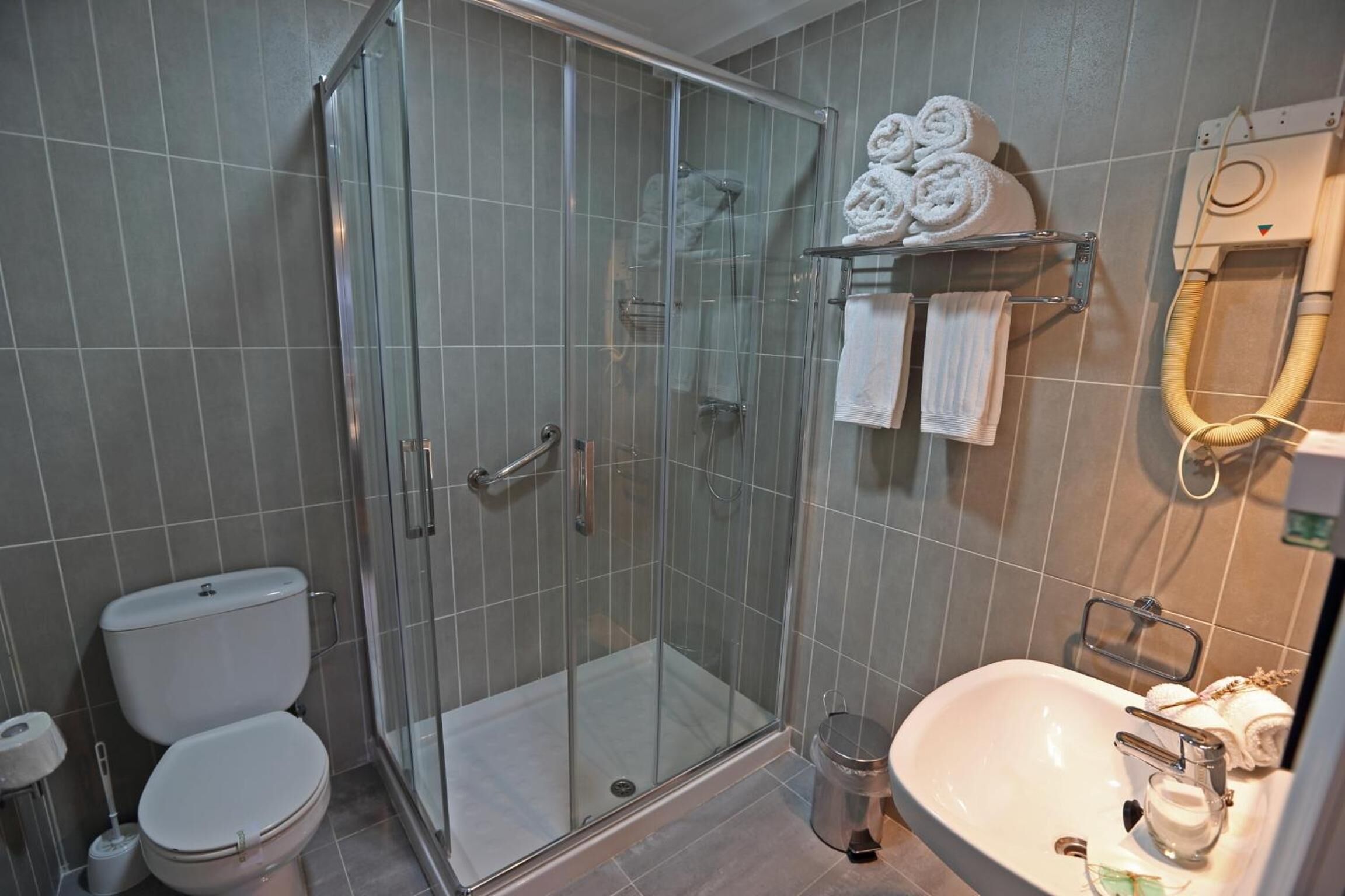 Un baño moderno con ducha de vidrio, inodoro y lavamanos con espejo.