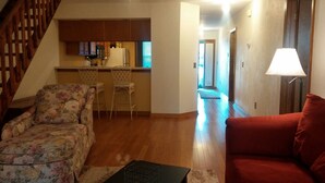 Ein Wohnzimmer mit einem floralen Sessel, einem roten Sofa und einer Küchenzeile mit Holzschränken und einem Kühlschrank.