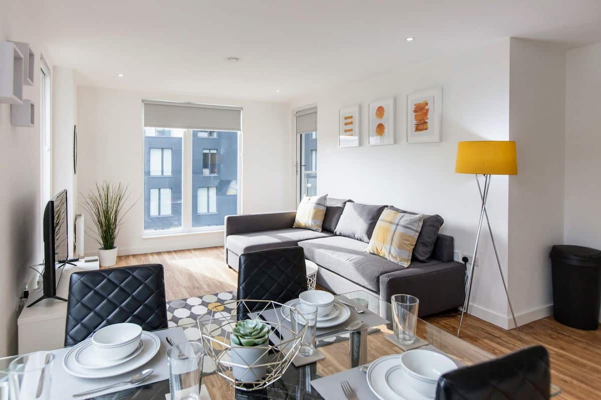 A modern living room with a dining area, a sofa set, and a large window with a view of buildings.
