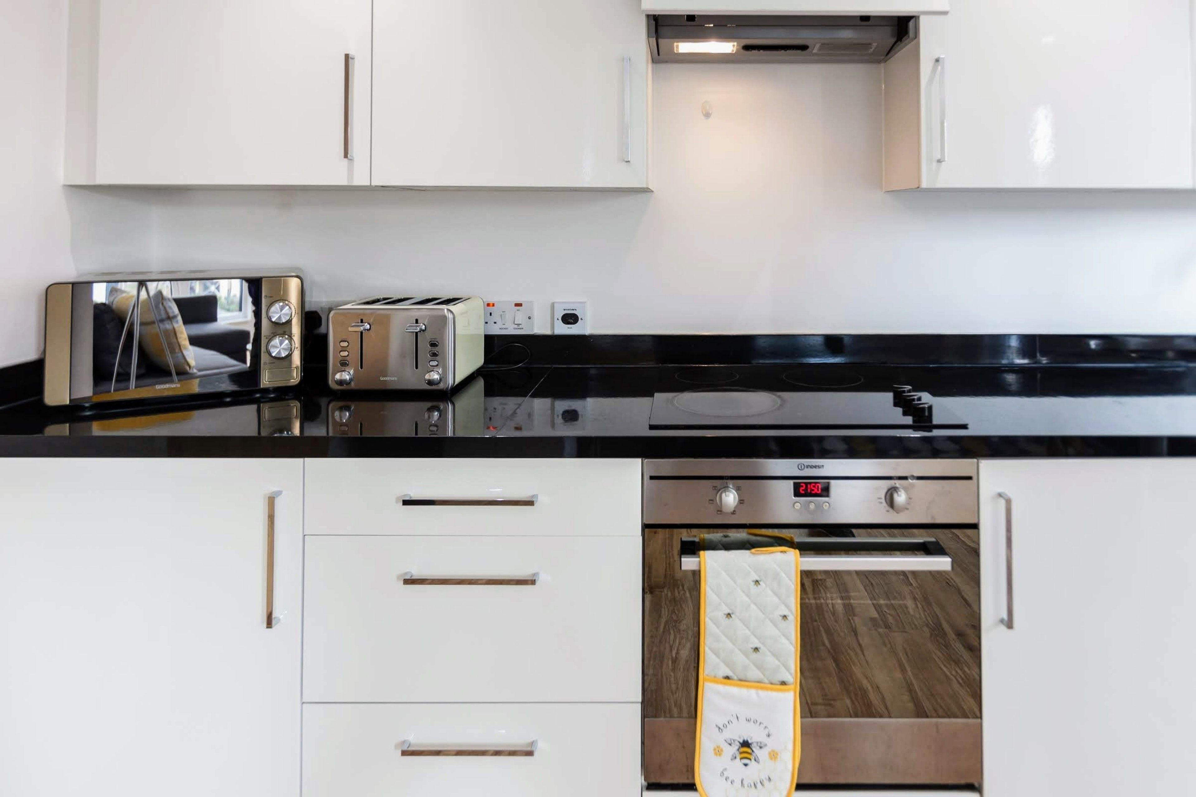 Een moderne keuken met witte kasten, een zwart aanrecht, een broodrooster, een magnetron en een oven.