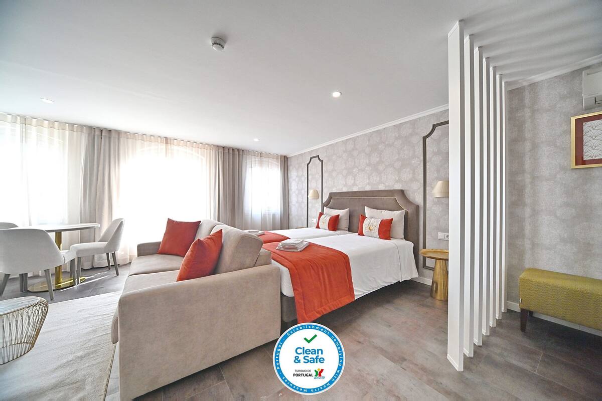 Quarto de hotel com cama, dois sofás, mesa de jantar e um banquinho.