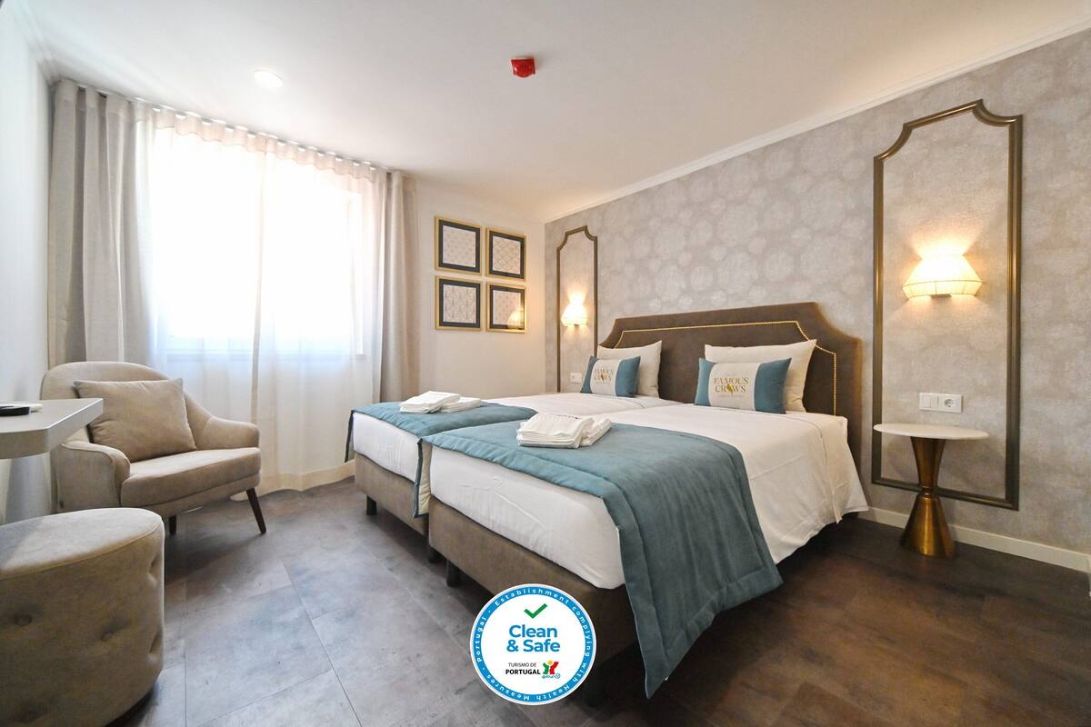Quarto de hotel com duas camas, um espaço de estar com uma poltrona, uma mesa e um espelho grande.
