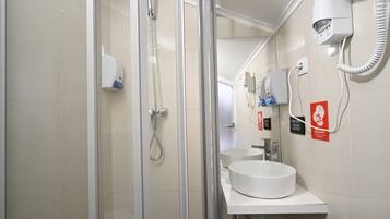 Un baño moderno con cabina de ducha de vidrio, un lavamanos blanco y un secador de pelo montado en la pared.