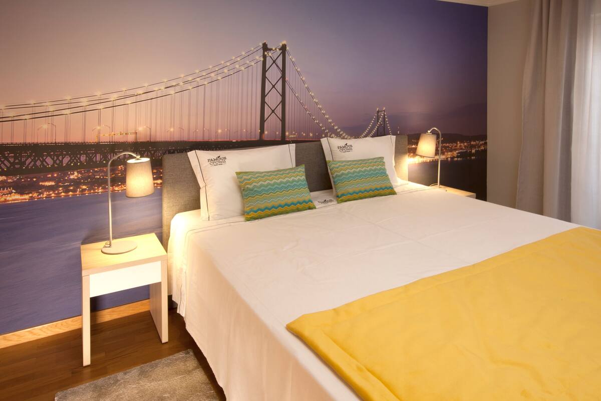 Quarto de hotel com uma cama, mesas de cabeceira e um grande mural na parede retratando uma ponte.