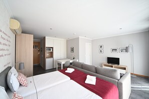 A modern hotel room with a bed, two sofas, a desk, a television, and a kitchenette. - Famous Crows Lisbon Suites (Lisbon)