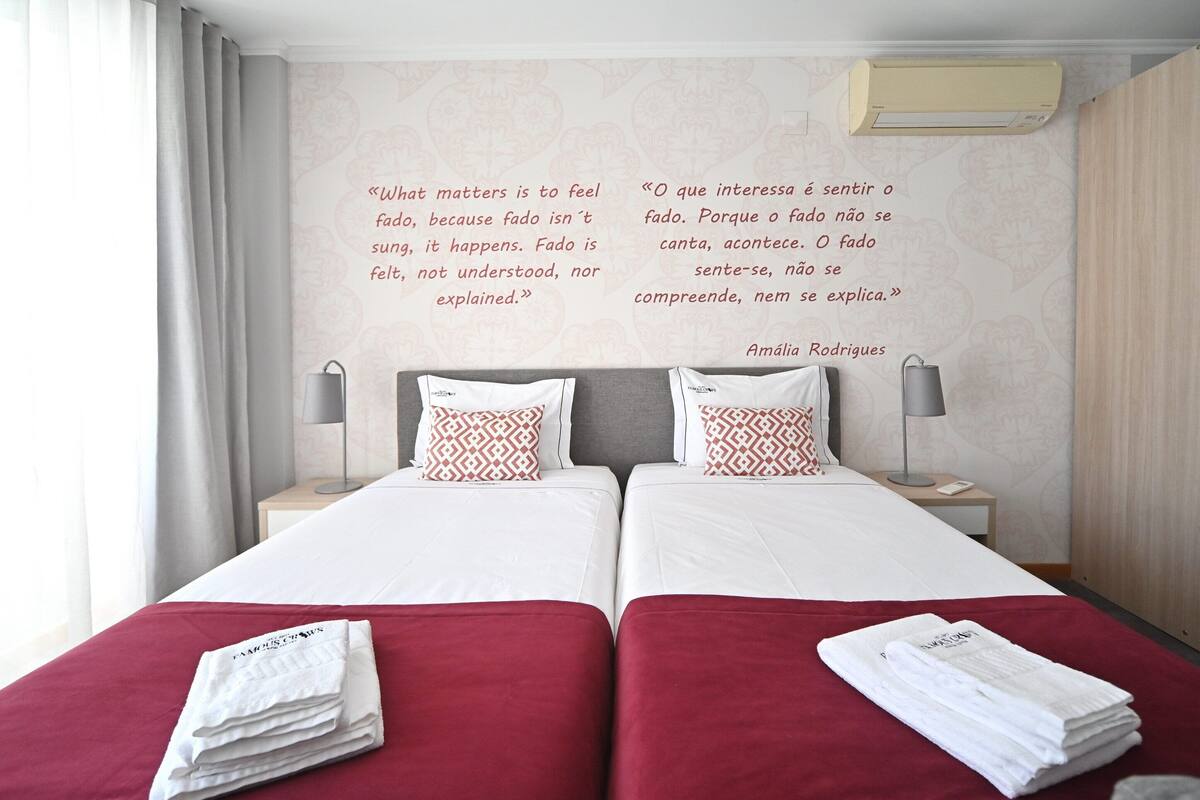 Quarto de hotel com duas camas, esquema de cores vermelho e branco e uma frase na parede.