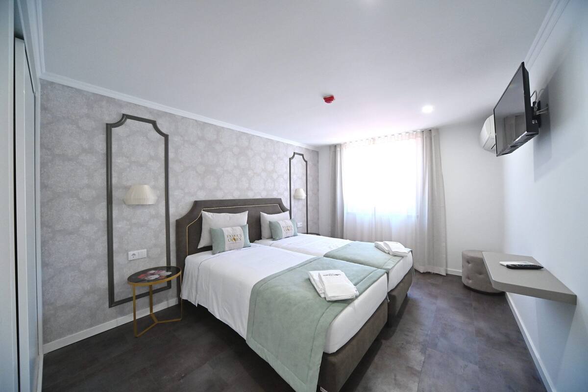Quarto de hotel com duas camas, uma mesinha, televisão e janela com cortinas.