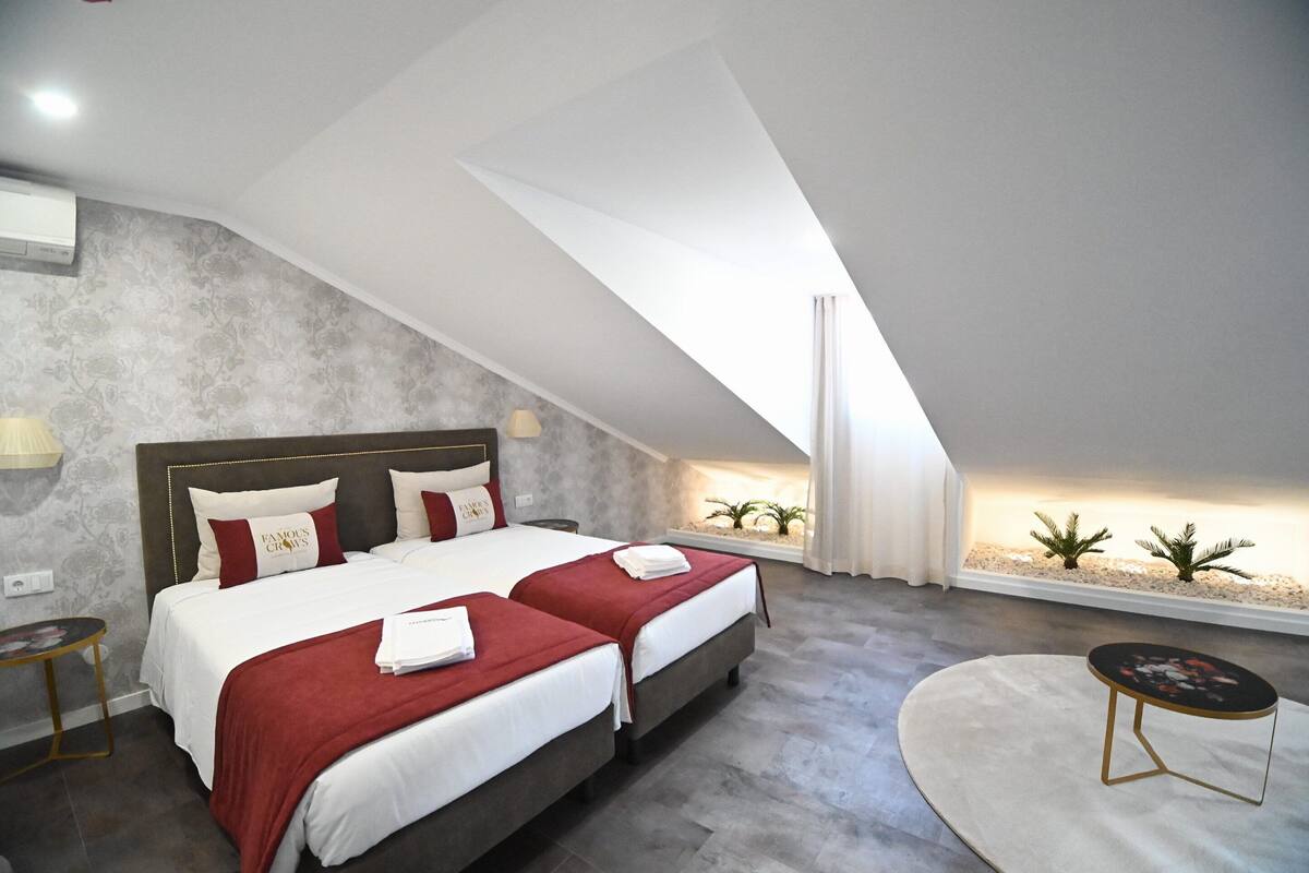 Quarto moderno com duas camas, uma mesa redonda e um espaço com plantas.