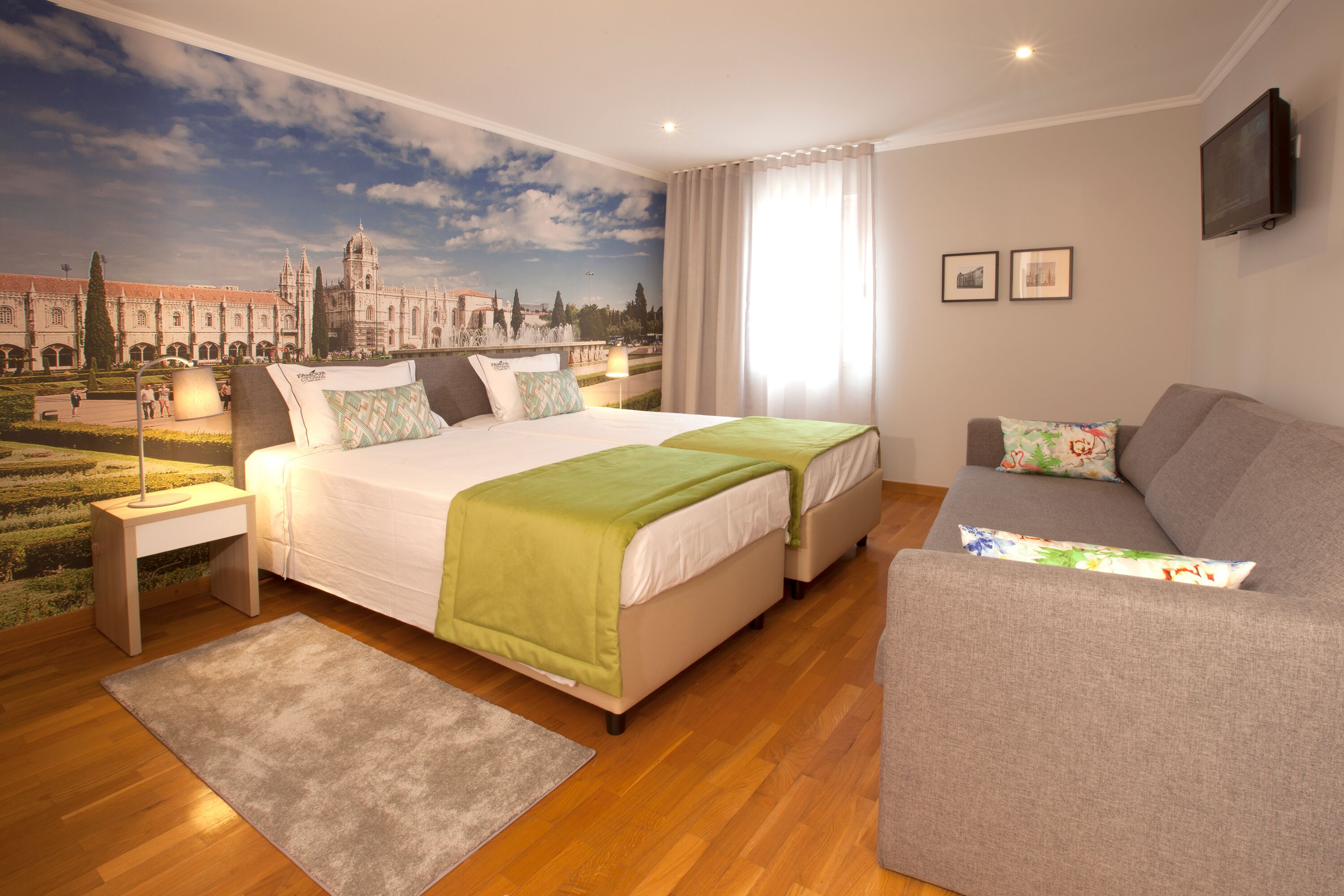 A hotel room with a large bed, a sofa, a nightstand, and a mural of a historic building.