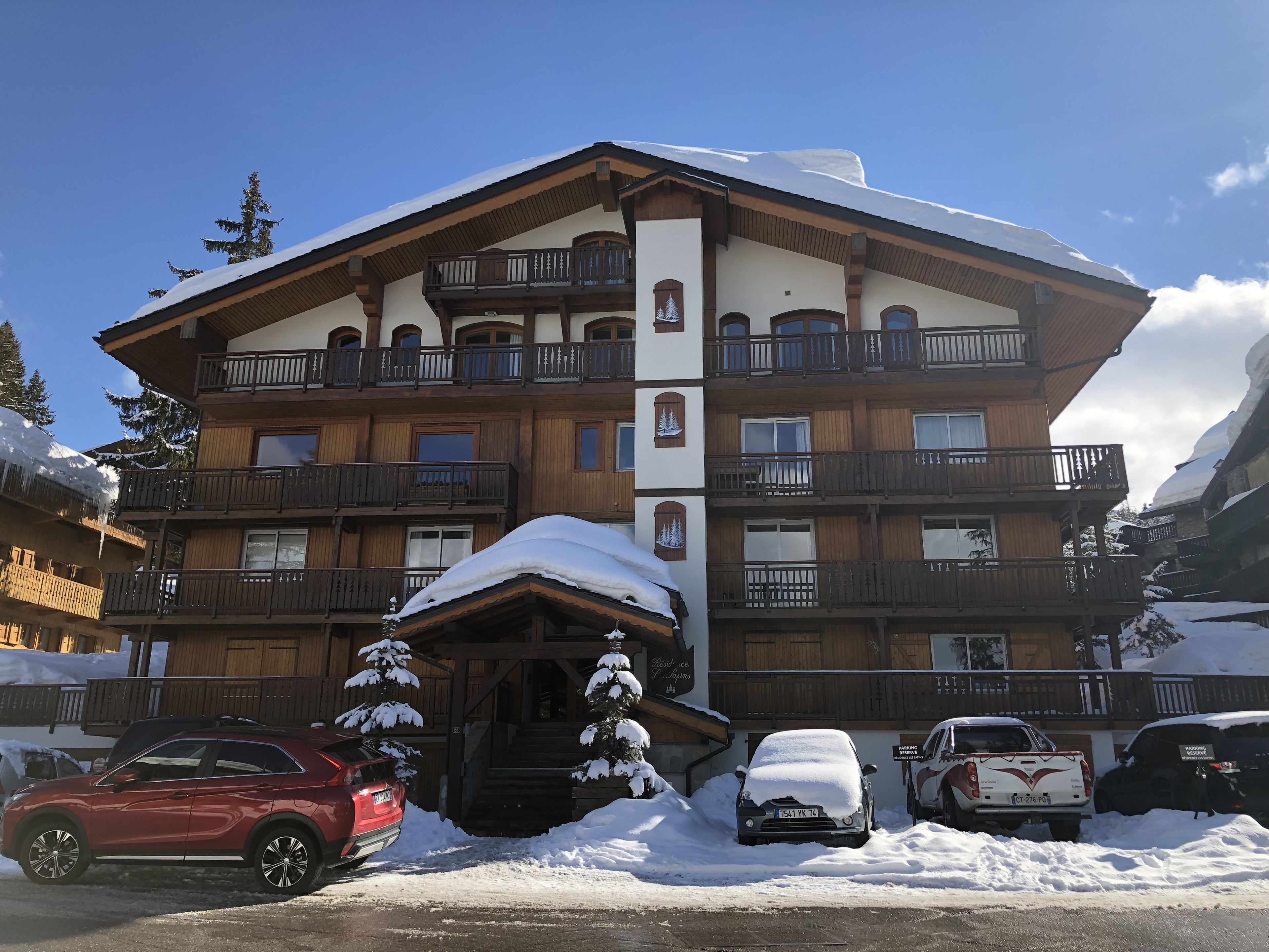 Un hotel de varios pisos con balcones, una entrada cubierta y paisajes nevados.