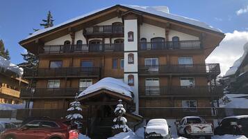 Un hotel de varios pisos con balcones, una entrada cubierta y paisajes nevados.