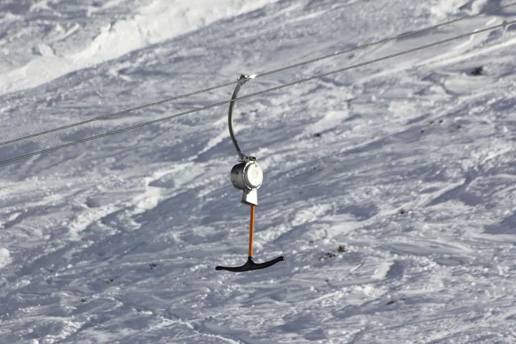 Silla de telesilla suspendida por un cable sobre una ladera nevada.