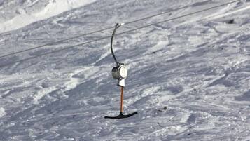 Silla de telesilla suspendida por un cable sobre una ladera nevada.