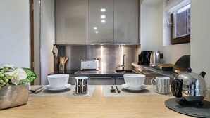 Una cocina moderna con electrodomésticos de acero inoxidable, una cafetera y un comedor con una mesa dispuesta para dos.