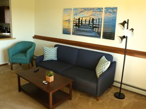 A living room with a dark blue sofa, teal armchair, wooden coffee table, and a floor lamp.