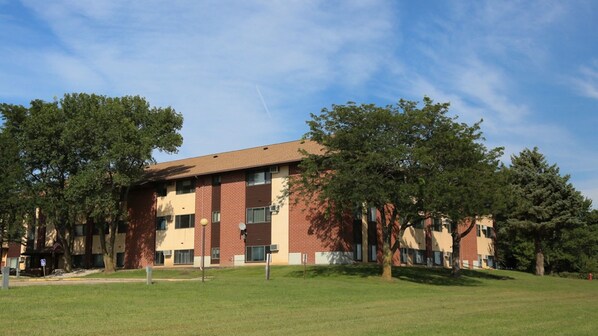 A multi-story brick building with a flat roof, surrounded by a grassy area and trees.
