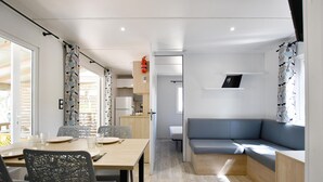 A modern, compact living space with a dining area, kitchenette, and a seating area with a sofa and a small table. - Camping Bella Vista (Calvi)
