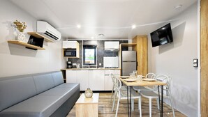A modern kitchen with built-in appliances, a dining area with a wooden table and chairs, and a grey sofa. - Camping Bella Vista (Calvi)