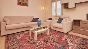 Un salon avec un canapé beige, une table basse en verre et un tapis à motifs.