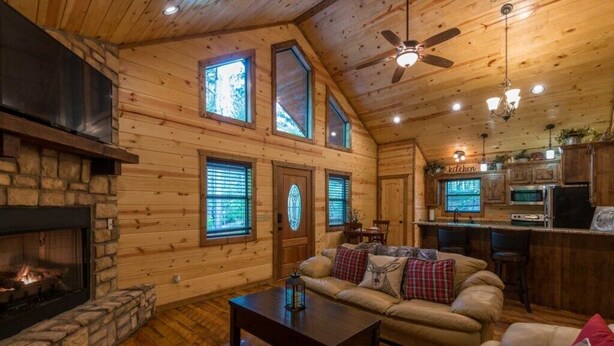 A cozy cabin interior with a stone fireplace, a leather sofa, and a kitchen area.