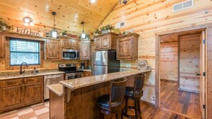 A wooden cabin kitchen with a granite countertop, wooden cabinets, a refrigerator, a microwave, and a sink.