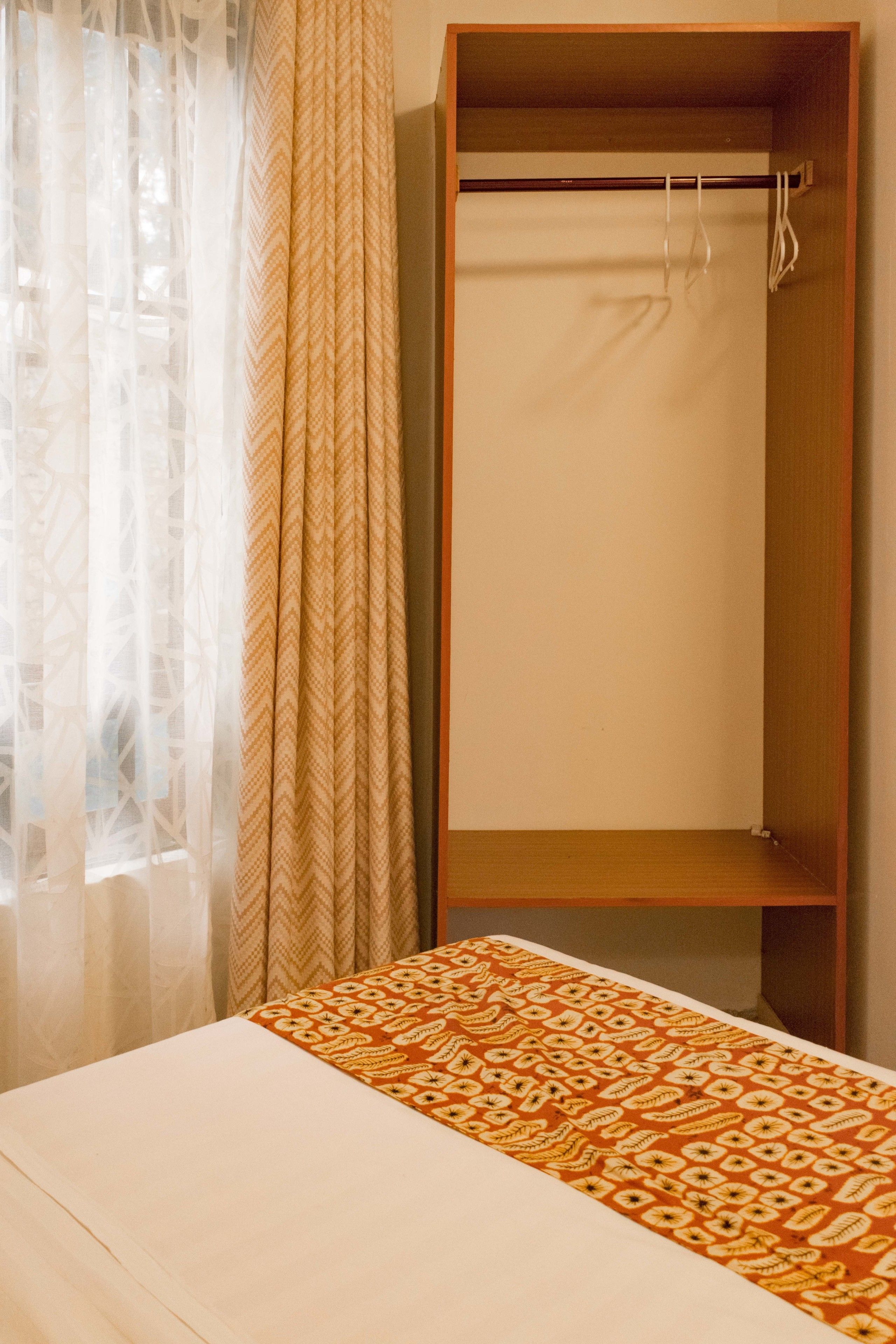 Une chambre avec un lit, une armoire en bois et une fenêtre ornée de rideaux légers.