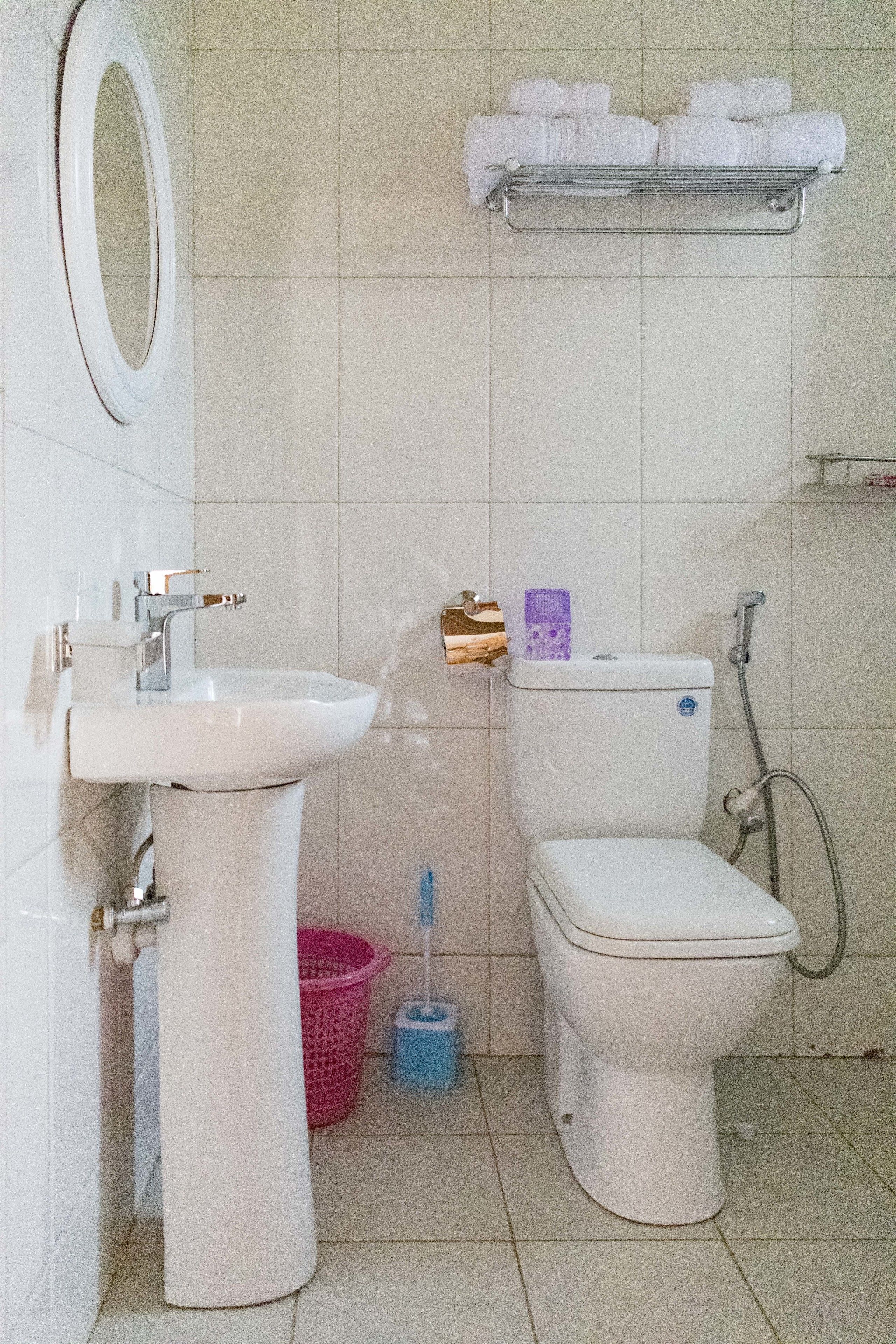 A bathroom with a sink, toilet, and a shelf above the toilet holding towels.