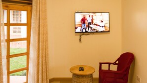 A room with a television mounted on the wall, a wicker table, a red chair, and a window with curtains. - Tooro Fairway Hotel (Fort Portal)