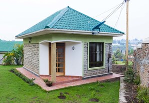 A small house with a green roof, a stone exterior, and a small garden.