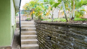 A staircase leading to a building with a green exterior wall, a stone retaining wall, and tropical plants. - Tooro Fairway Hotel (Fort Portal)