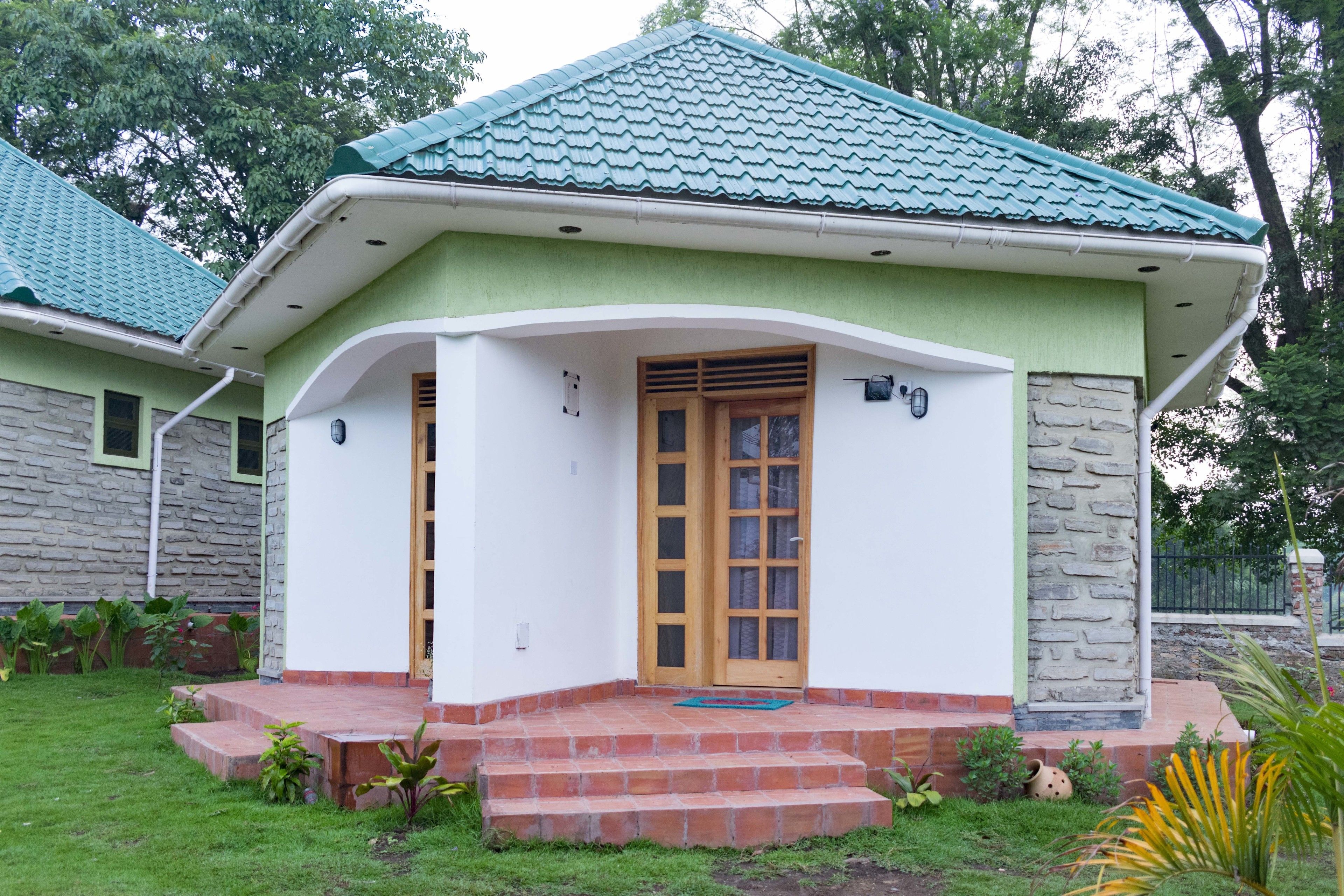 Una casa con techo verde, un porche delantero y un muro de piedra.