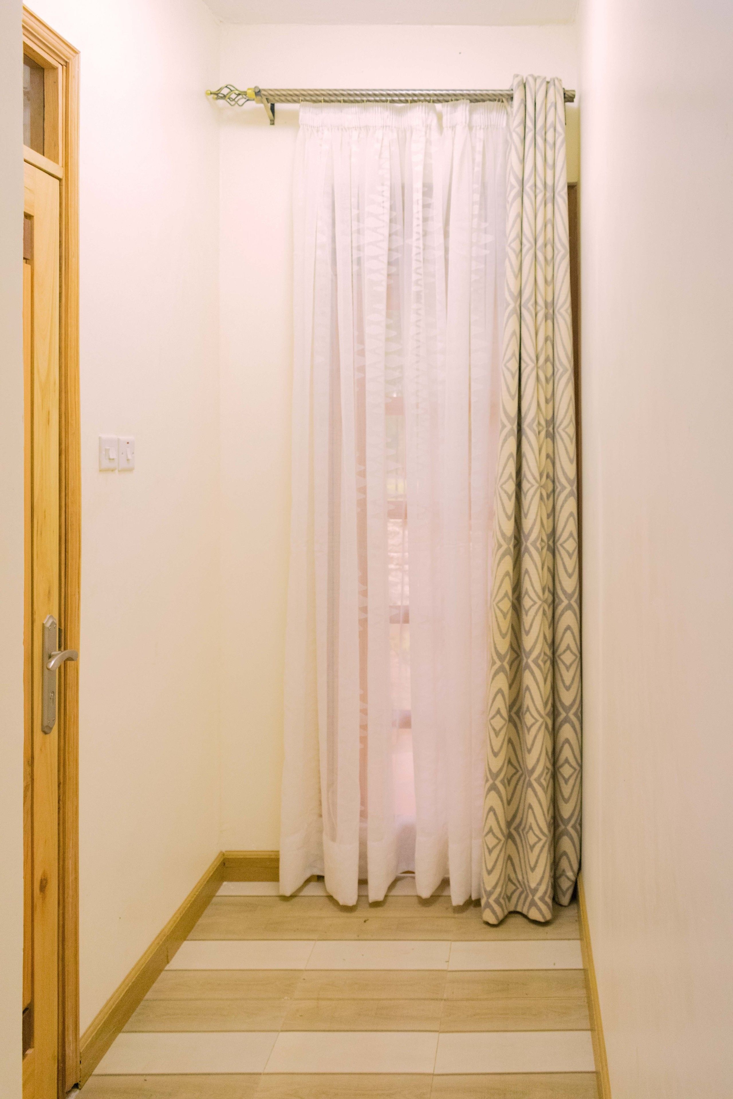 Un pasillo estrecho con una puerta de madera a la izquierda y una cortina de ducha con un diseño geométrico a la derecha.