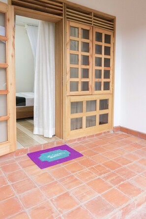 A room with a bed, a wooden door, and a purple mat on the floor.