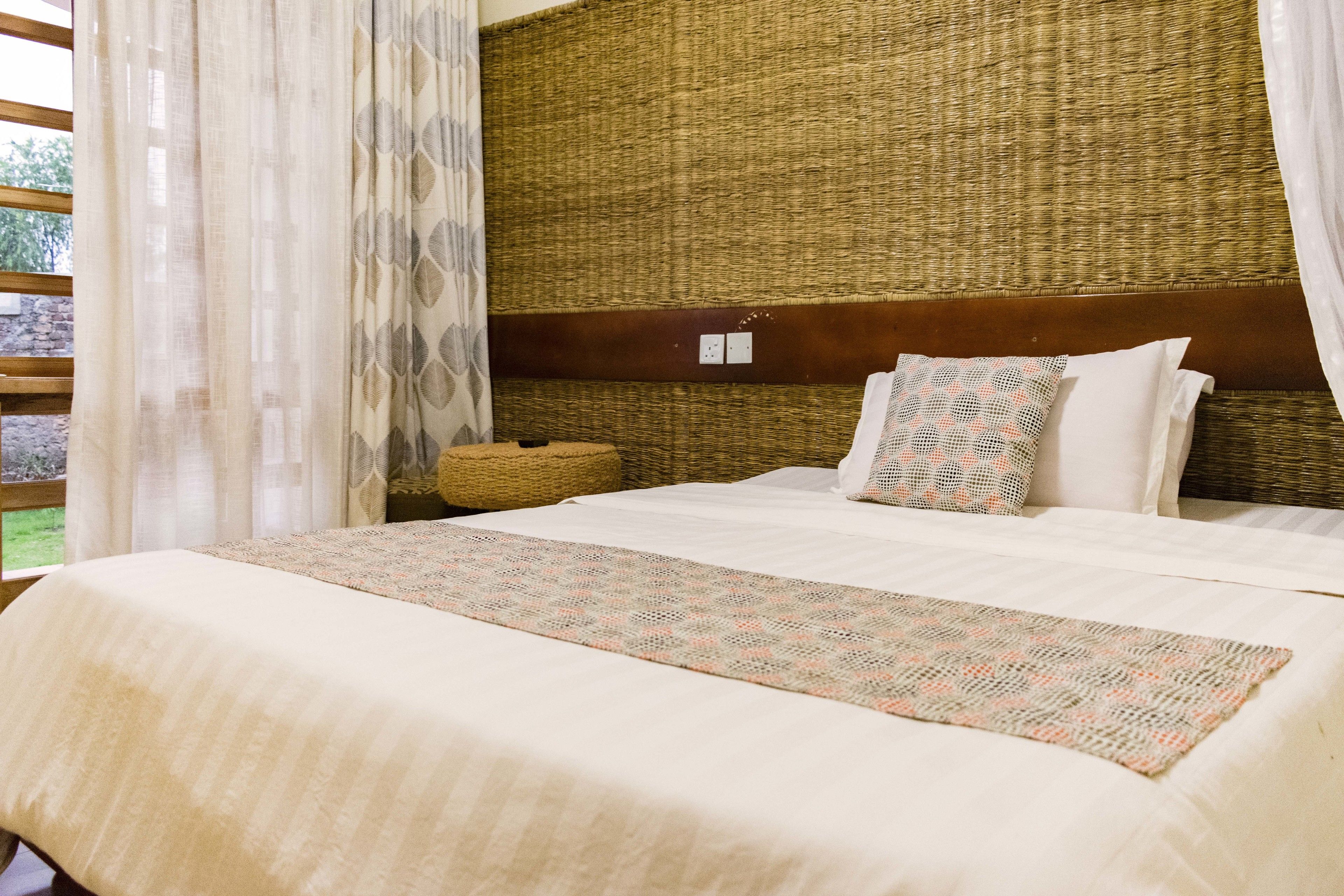 Une chambre avec un grand lit, une tête de lit en osier et une vue sur l’extérieur.