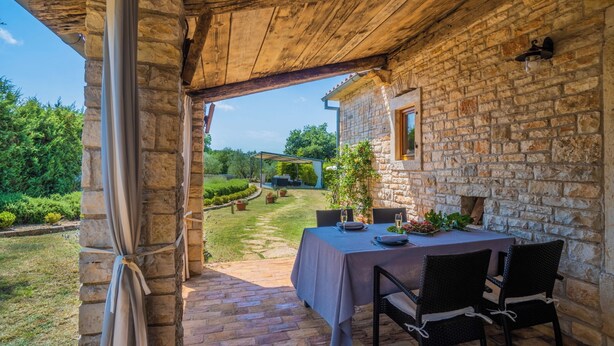 Ein Steinhaus mit einer überdachten Terrasse, einem gedeckten Tisch und Blick auf den umliegenden Garten.