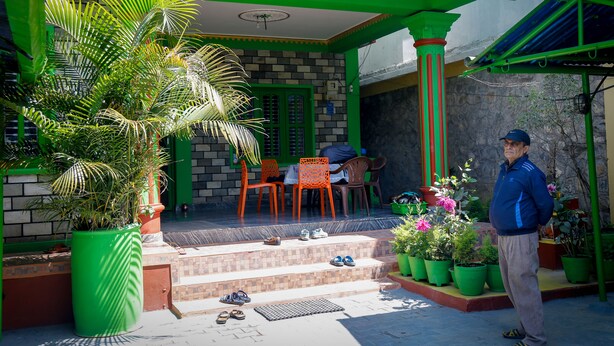 Una casa amb façana verd, un porxo amb cadires i una planta en test.