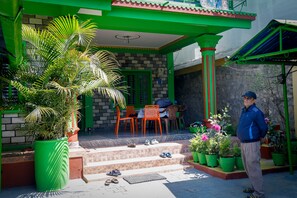 Una casa amb façana verd, un porxo amb cadires i una planta en test.
