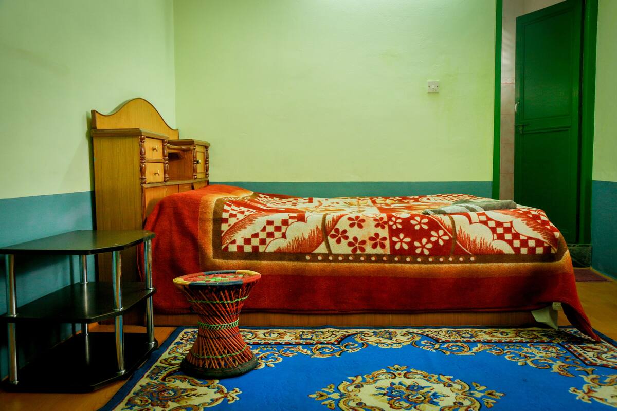 A room with a bed, a small table, a chair, and a decorative basket.