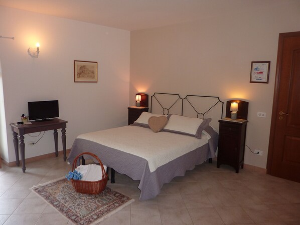 Un dormitorio con cama, mesitas de noche, un escritorio con televisor, una lámpara de pared y una puerta.