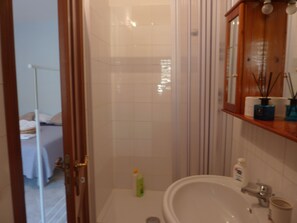 Un baño con lavamanos blanco, espejo y zona de ducha.