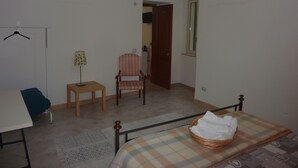 A room with a bed, a chair, a table, a hanging rack, and an air conditioning unit. - Duomo Rent Room & Flat (Agrigento)