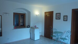 A room with a refrigerator, a window with blinds, a door, and a small table with chairs. - Duomo Rent Room & Flat (Agrigento)