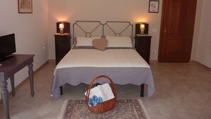 A neatly arranged bedroom with a bed, two bedside tables with lamps, a television on a side table, a door, and a decorative basket on the floor. - Duomo Rent Room & Flat (Agrigento)