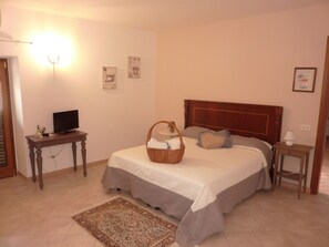 Un dormitorio con cama, televisión sobre una mesita auxiliar, lámpara de noche y luz en la pared.